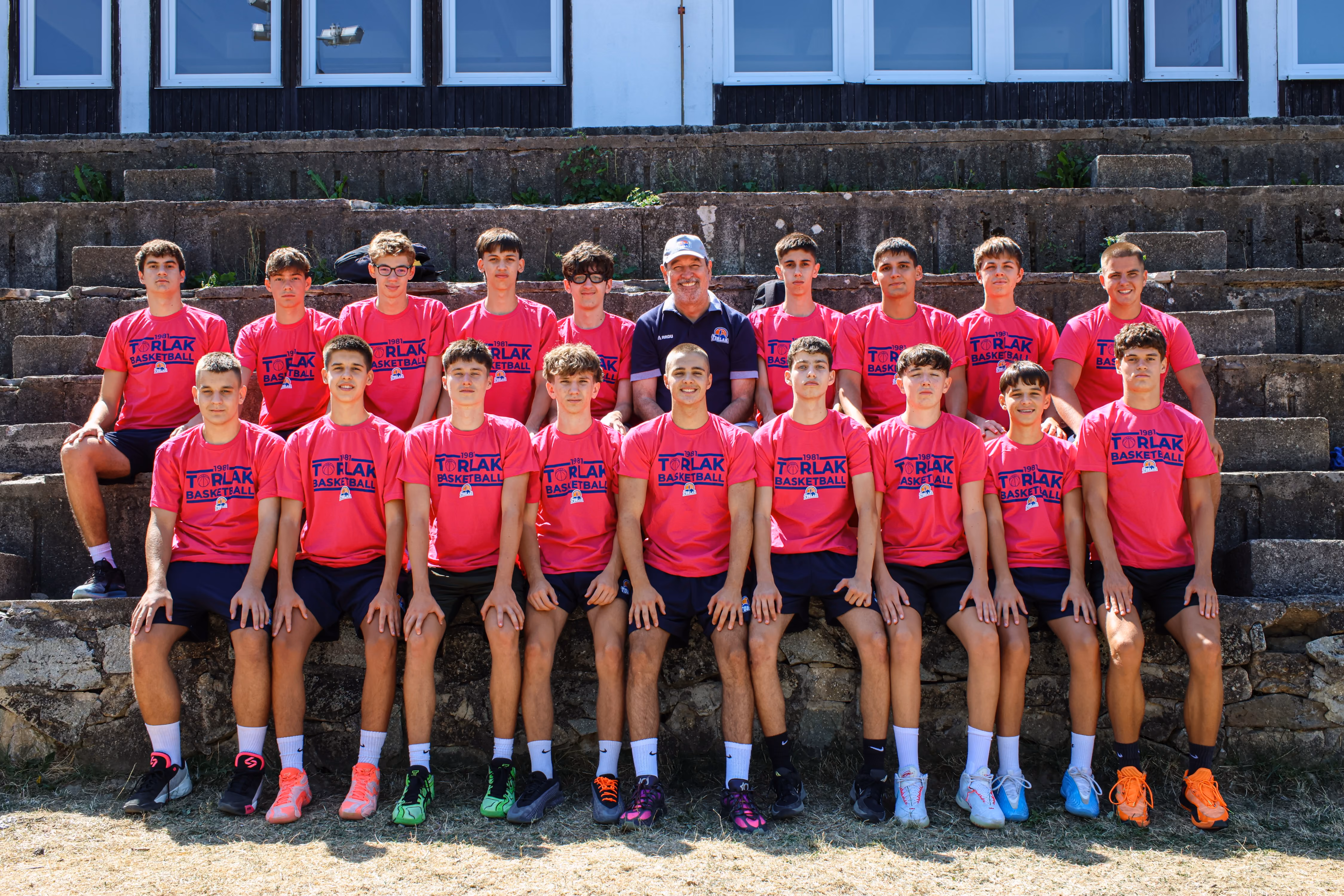 Basketball team of teenage boys and coach posing on an outdoor court in matching uniforms.