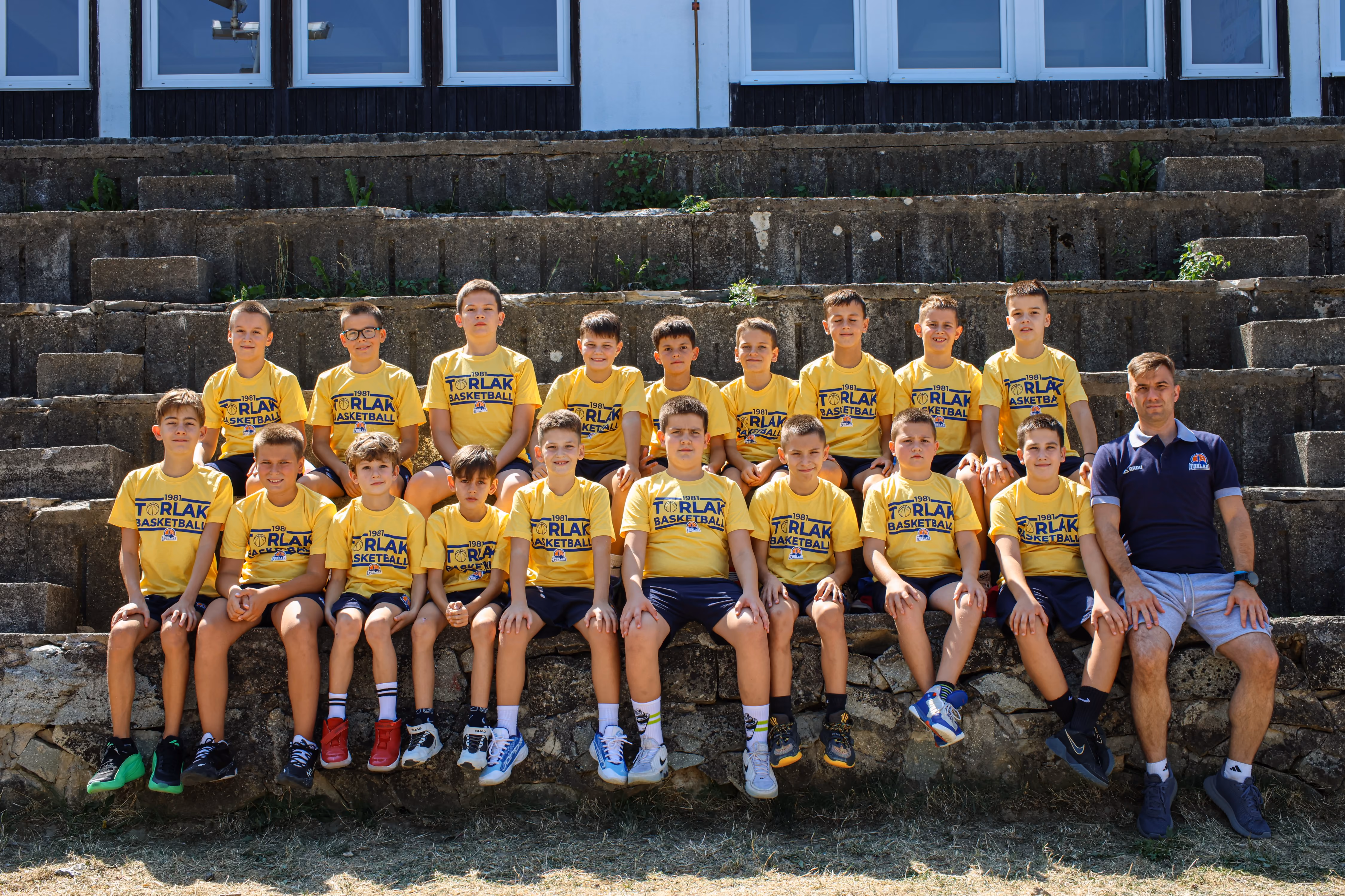 Youth basketball team in white shirts and blue shorts posing with coach on outdoor court.